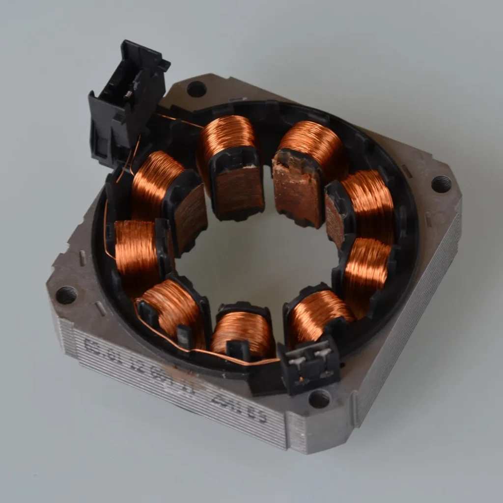 Stator de moteur électrique démonté, bobinages de cuivre à nu, posé sur fond neutre
